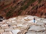 Traveler in a blue dress walking among the white salt pools of the Maras salt mines