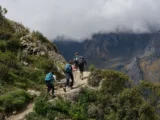 Trekkers hiking a mountain trail with backpacks and poles toward Humantay Lake, clouds over the peaks