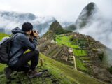 Hiker taking photos of Machu Picchu ruins with Huayna Picchu peak wrapped in clouds