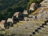 Restored thatched-roof houses and stone terraces at Machu Picchu with visitors exploring