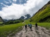 Hikers trekking across a green valley toward Humantay Lake with grazing horses nearby
