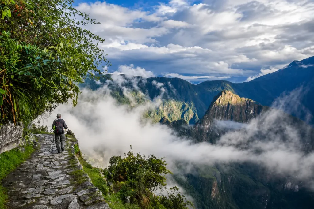 Hiker descending stone steps from Inti Punku, the Sun Gate, on the Inca Trail with Machu Picchu below