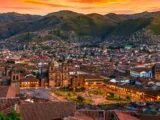 Panoramic view of Cusco at sunset with the lit Plaza de Armas, the cathedral and hills covered in houses behind