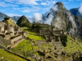 Sunlit Machu Picchu citadel with visitors walking the terraces and Huayna Picchu wrapped in cloud behind