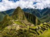 Wide view of Machu Picchu from the upper terraces with Huayna Picchu and cloud-covered peaks behind