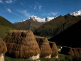 Row of thatched andean huts under a starry sky with the snow-capped Salkantay range lit by moonlight