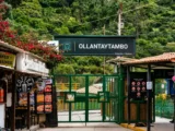Green gate and sign of the Ollantaytambo train station with small shops and bougainvillea at the entrance