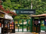 Green gate and sign of the Ollantaytambo train station with small shops and bougainvillea at the entrance
