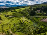 Aerial view of the Puka Pukara fortress on a green hill beside the road out of Cusco, with the valley and mountains behind
