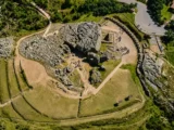 Aerial view of a carved rock outcrop with visitors and curved stone terraces inside the Sacsayhuaman archaeological park