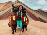 Turista sonriendo junto a dos llamas con lentes de sol en la Montaña de Colores