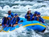 Smiling rafting team paddling a blue raft through rapids on the Inca Jungle Trail