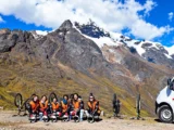 Downhill mountain bike group at a high Andean pass with a snowy peak on the Inca Jungle Trail