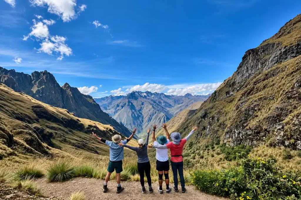 Hikers celebrating at a high Andean pass on the Inca Trail with a deep valley below