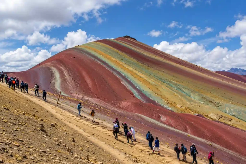 Hikers climbing the dirt trail toward the Rainbow Mountain summit in thin mountain air