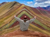 Wanderer mit erhobenen Armen vor den Farbstreifen des Regenbogenbergs in Peru